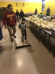 A child pushing a broom marvels at a table full of produce.