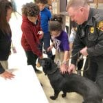 A child pets a police dog at a school.