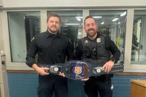 Officer Ratliff and Officer Miller standing side by side indoors, smiling and holding a decorative championship-style belt recognizing them as Second District Officers of the Month.