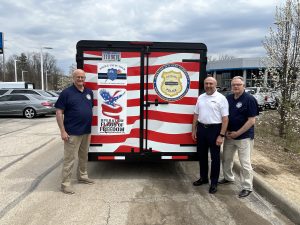 Group photo at the rear of the trailer with all supporting logos visible, including CPF and Flags of Freedom; Bob Guttu and Rick DeChant are pictured.