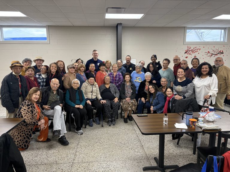 Second District officers pose with a large group of seniors and staff gathered for a group photo at the Hispanic Senior Center.