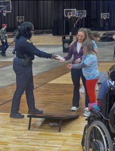 Officer hands beanbags to young athletes during a cornhole game.