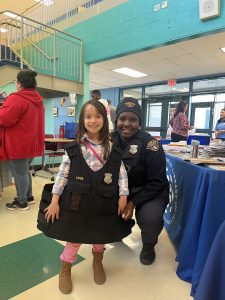 Officer Lavender kneels beside a young girl proudly wearing CPD gear