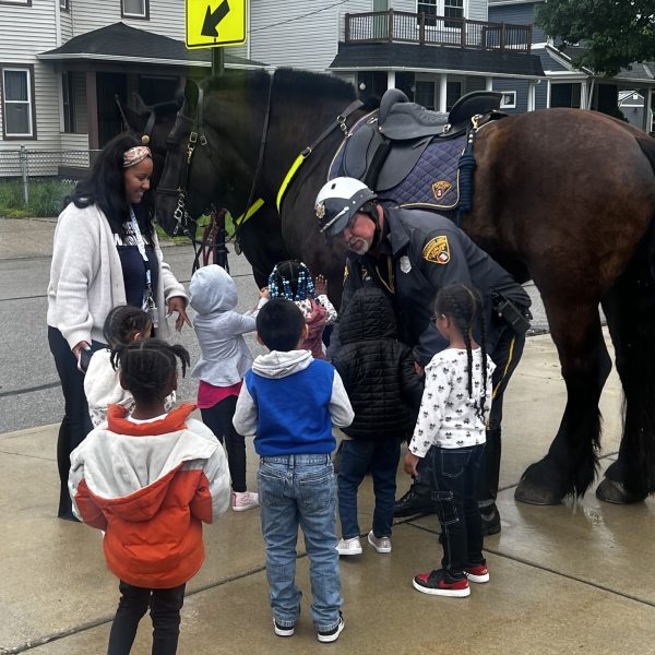 Mounted Unit officer introduces children to one of the patrol horses while students and staff gather around.