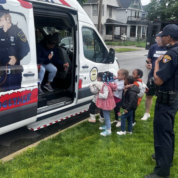 Kids talk with officers near the community outreach van decorated with cartoon-style police art.