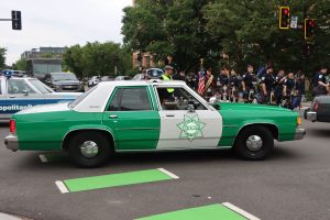 Vintage sheriff’s patrol car drives past as out-of-town police pipe bands line up in the background