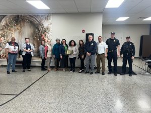 Group photo of CPD Second District officers with staff and members of the Hispanic Senior Center, including Commander Maffo-Judd and Bob Guttu, holding a Community Partner of the Month plaque