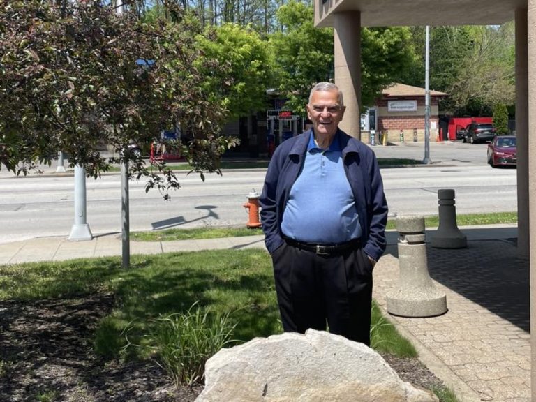Alex Machaskee stands beside a stone engraved with "Servant’s Heart" outside the University Circle Police Department on a sunny day