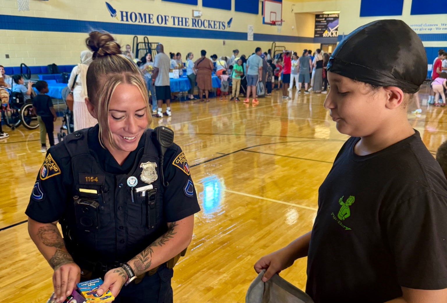 Back to School at RG Jones - Feature An officer smiles while giving a pack of crayons to a student holding a drawstring bag during the school supply event at RG Jones School.