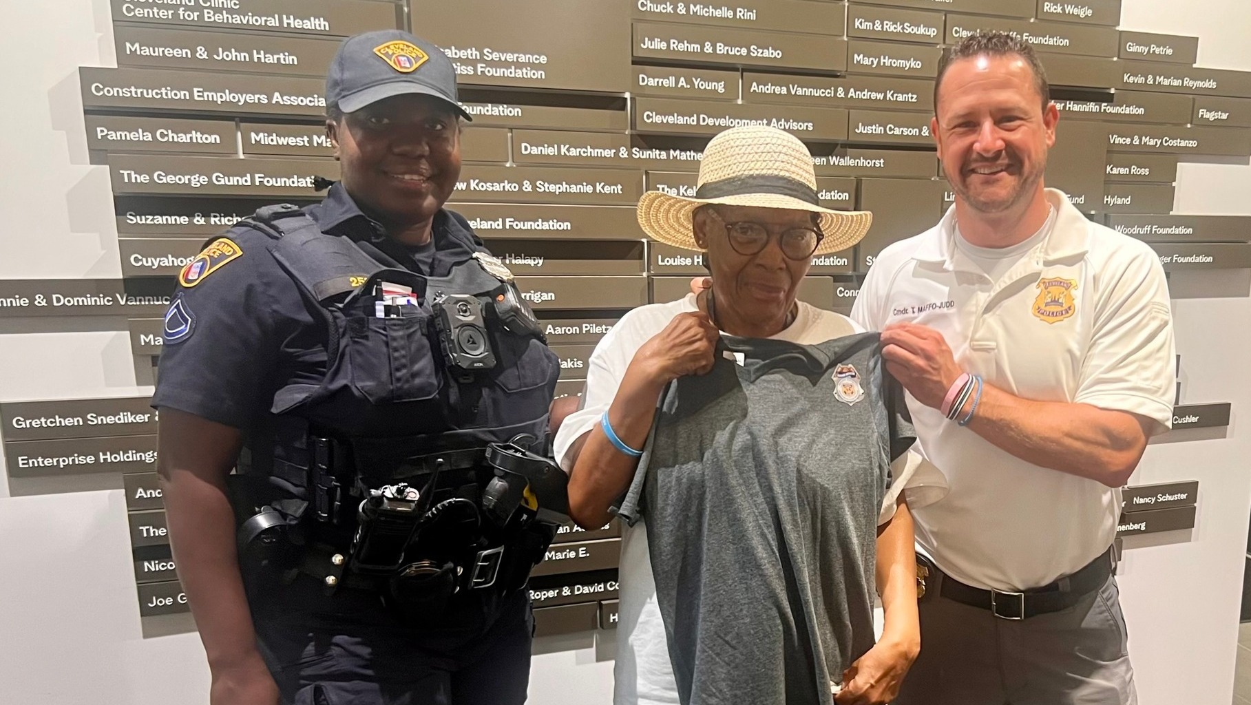 May Dugan Center Donations Second District officer and commander present a Cleveland Police T-shirt and badge to a smiling senior resident inside the May Dugan Center.